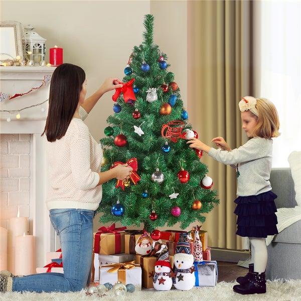 Familie schmückt künstlichen Weihnachtsbaum mit Christbaumkugeln und Schleifen, Geschenke unter dem Baum