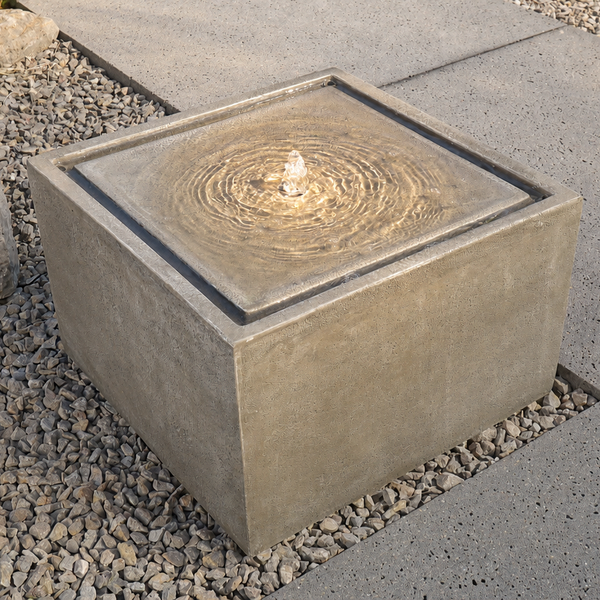 Quadratischer Gartenbrunnen in Steinoptik mit sprudelndem Wasser und integrierter LED-Beleuchtung auf einer Terrasse.
