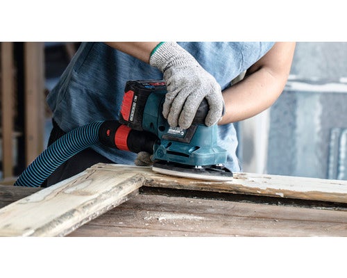 Eine Person schleift Holz mit einem Exzenterschleifer und Staubsaugeranschluss.