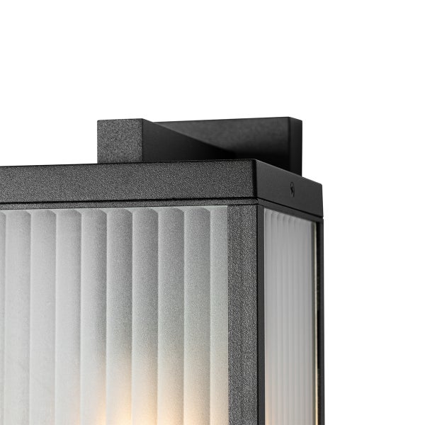 Nahaufnahme einer schwarzen Außenwandleuchte mit geriffeltem Glas und Metallrahmen.