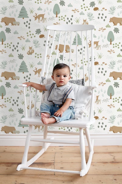 Ein Baby sitzt in einem Schaukelstuhl vor einer Tapete mit Waldmotiven.