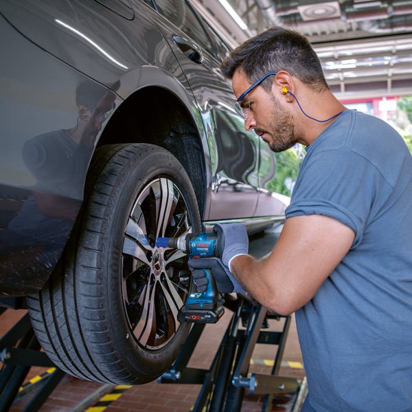 Ein Mechaniker benutzt einen Akku-Schlagschrauber von Bosch, um ein Rad an einem Auto in einer Werkstatt zu wechseln.