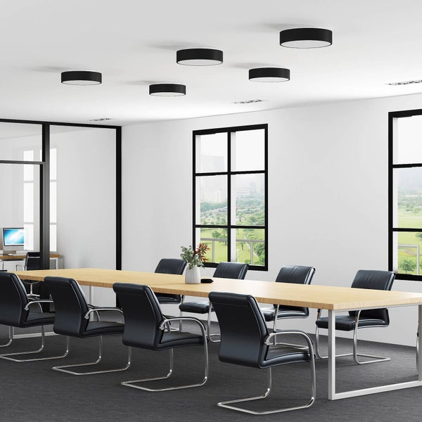 Heller Konferenzraum mit langem Holztisch, schwarzen Bürostühlen und fünf runden schwarzen Deckenleuchten in einer organisierten Atmosphäre.
