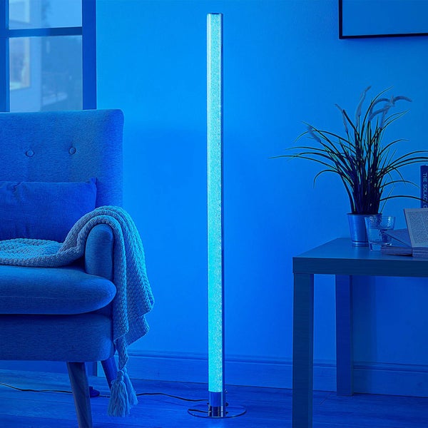 Schlanke, zylindrische LED-Sprudelsäule als Stehleuchte in einem modernen Wohnzimmer neben einem Sessel und einem Beistelltisch.