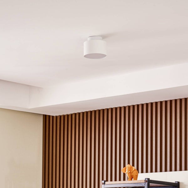 Moderne weiße zylindrische Deckenleuchte an der Decke über einer Wand mit vertikalen Holzlamellen.