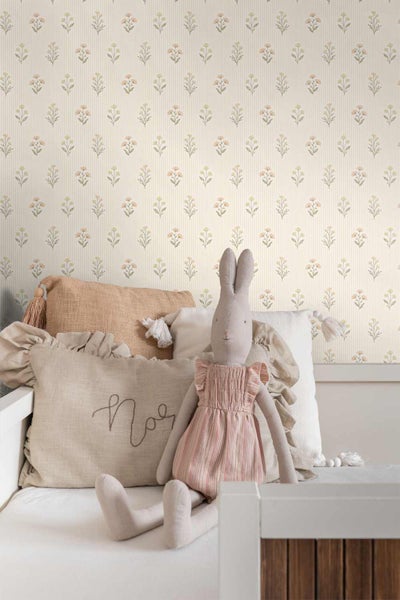 Tapete mit floralem Muster und feinen vertikalen Streifen in einem hellen Kinderzimmer mit dekorativen Kissen und einem Stoffhasen auf dem Bett.