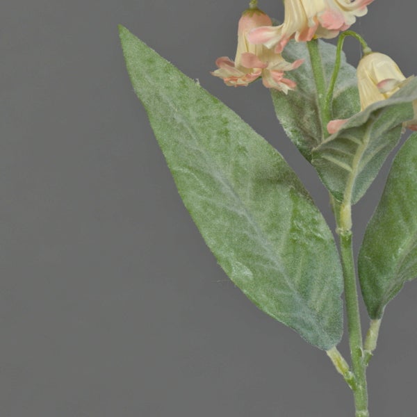 Nahaufnahme eines künstlichen Blütenzweigs mit samtigen grünen Blättern und cremefarbenen glockenförmigen Blüten.