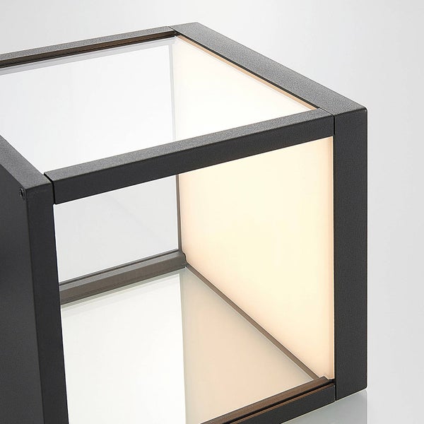 Nahaufnahme einer würfelförmigen Außenleuchte mit schwarzem strukturiertem Rahmen und warm leuchtenden Glasflächen.