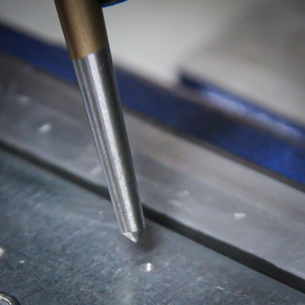 Ahle aus Metall sticht in eine Metallplatte