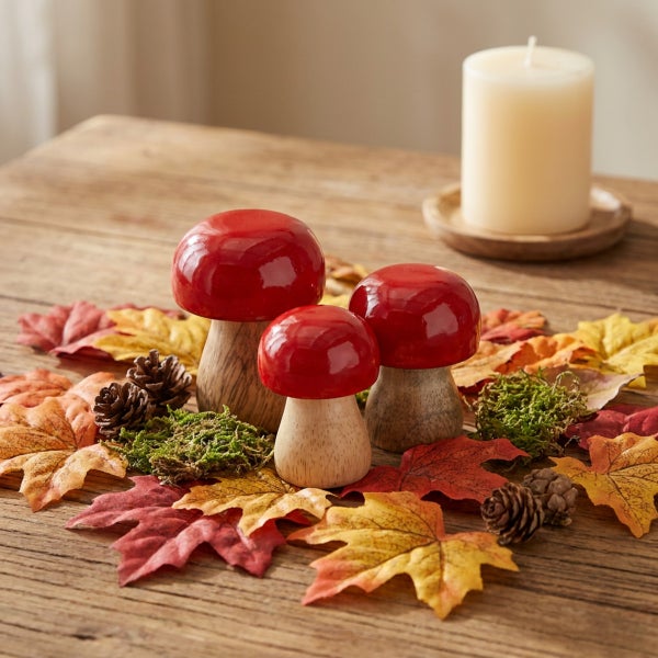 Drei dekorative Pilze aus Holz auf einem Tisch mit Herbstlaub und einer Kerze als herbstliche Tischdekoration