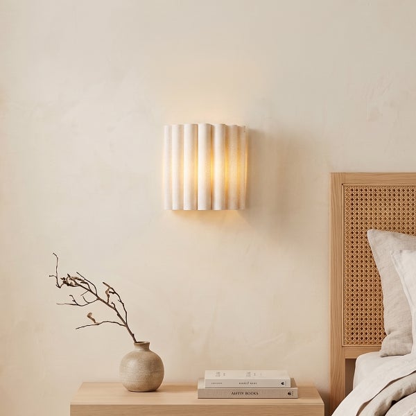 Wandleuchte mit gewelltem Design in einem Schlafzimmer mit Nachttisch, Vase und Bücherstapel.