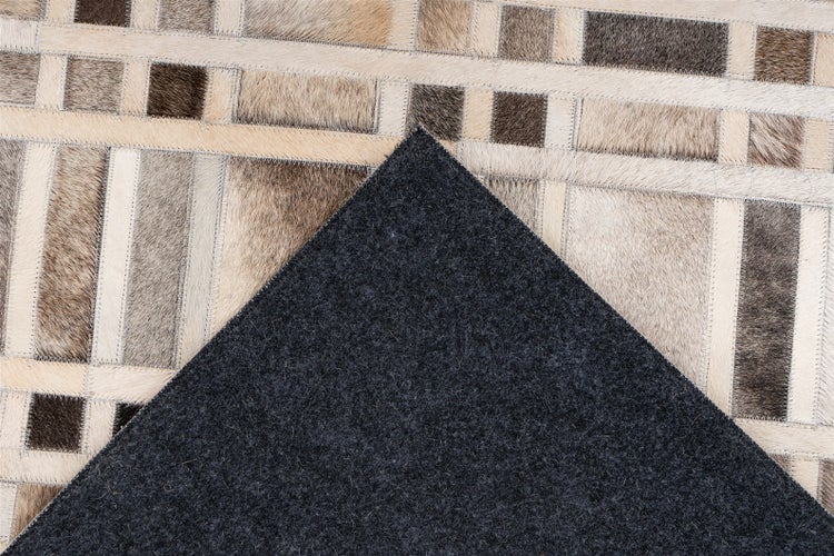 Patchwork-Kuhfellteppich aus rechteckigen Stücken mit einer dunkelgrauen Filzrückseite.