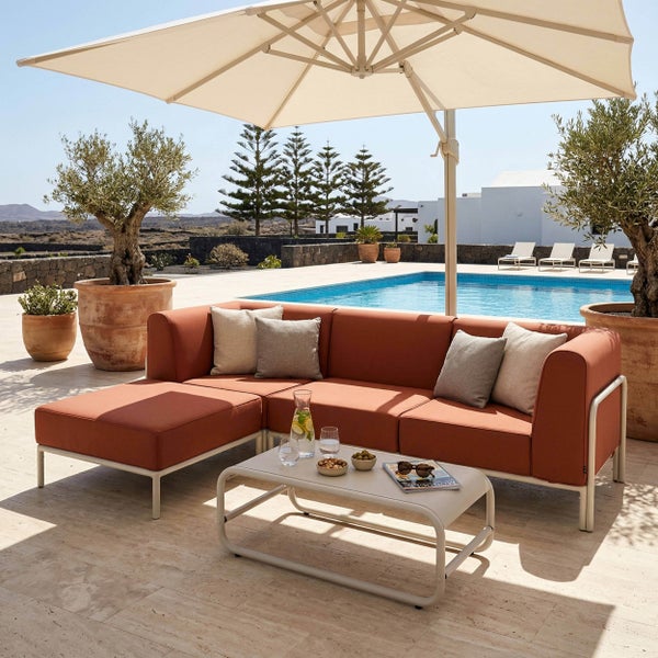 Moderne Gartenlounge-Ecke mit terrakottafarbenen Polstern, Couchtisch und großem Ampelschirm auf einer Terrasse neben einem Pool.