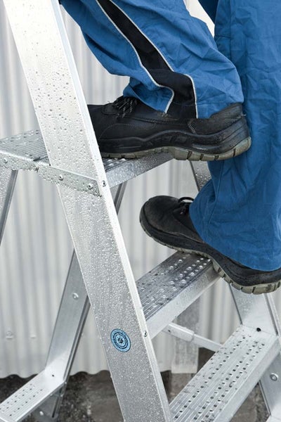 Person mit Arbeitsschuhen auf einer Aluminiumleiter