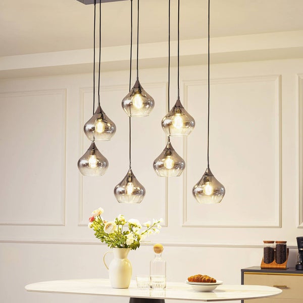 Siebenflammige Pendelleuchte mit tropfenförmigen Glasschirmen in verschiedenen Höhen über einem Esstisch in einem hellen Raum.