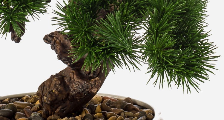 Nahaufnahme eines künstlichen Bonsai-Baums mit strukturierter Rinde, grünen Nadeln und Zierkies im Topf.