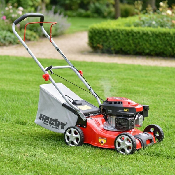 Benzin-Rasenmäher von Hecht mit rotem Gehäuse und grauem Fangkorb auf einer Rasenfläche im Garten.