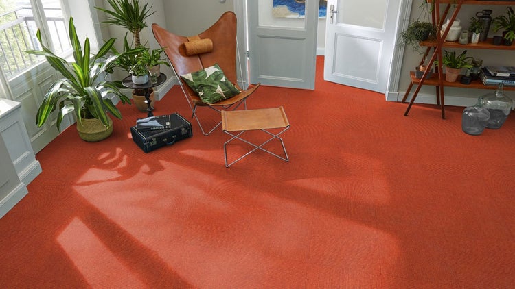 Wohnzimmer mit terracottafarbenen Teppichfliesen, einem ledernen Butterfly-Sessel, Zimmerpflanzen und hellem Lichteinfall.