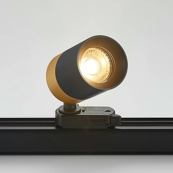 Moderner Schienensystem-Strahler in Schwarz und Gold, eingeschaltet auf einer schwarzen Schiene.