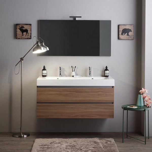 Moderner Waschtisch mit Holzfront und weißem Waschbecken an einer grauen Wand mit Spiegel, Stehlampe und dekorativen Wandbildern.
