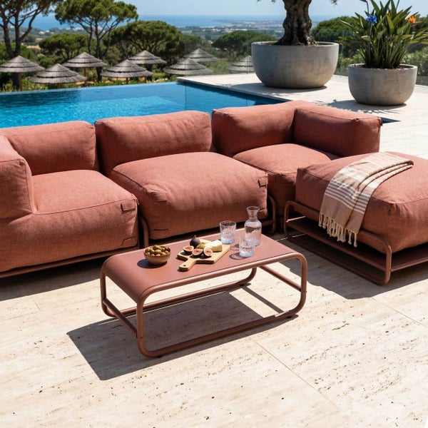 Moderner Lounge-Tisch aus Metall in Terrakotta auf einer hellen Terrasse mit passenden Gartenmöbeln, Snacks und Getränken.