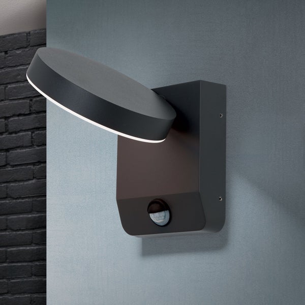 Moderne Außenwandleuchte mit neigbarem runden Lampenkopf und integriertem Bewegungsmelder montiert an einer Wand.
