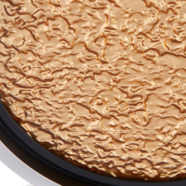 Detailansicht einer goldfarbenen, gehämmerten metallischen Oberfläche mit Wellenstruktur und dunklem Rand.