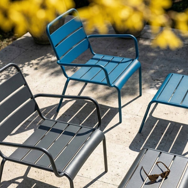 Moderne Garten-Lounge-Möbel aus Metall auf einer hellen Steinterrasse mit Sesseln und niedrigen Tischen in sonniger, organisierter Atmosphäre.