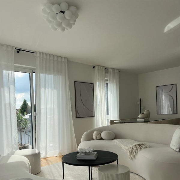 Helles Wohnzimmer mit Sofa, Vorhängen und Deckenleuchte