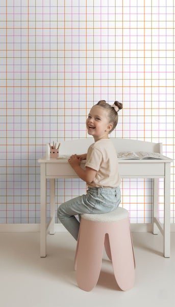 Weiße Tapete mit feinem buntem Karomuster in einem hellen Kinderzimmer hinter einem weißen Schreibtisch.