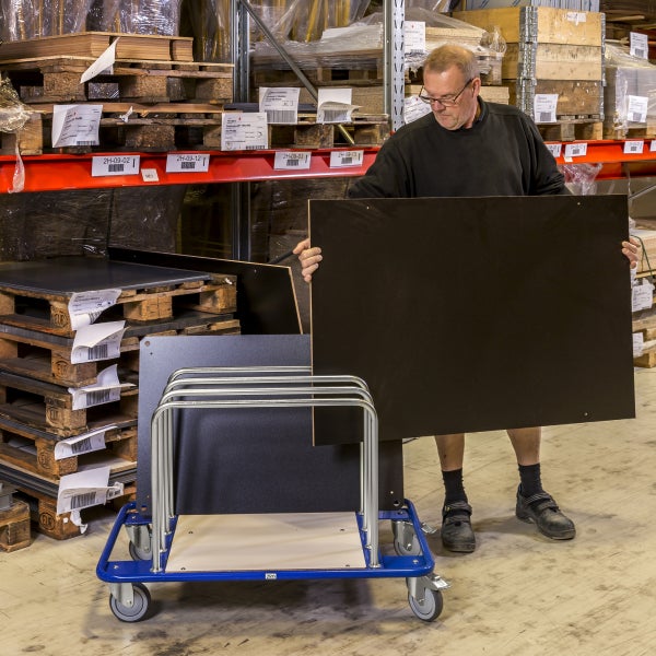 Mann hantiert mit einer Platte in einem Lager, daneben ein Transportwagen.