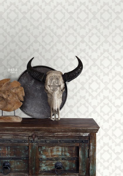 Dekoratives Stillleben mit Büffelschädel auf Kommode vor Tapete mit grafischem Muster