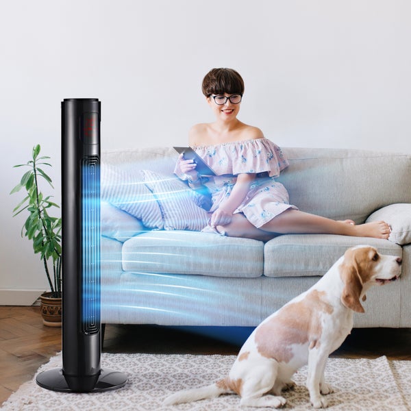 Moderner schwarzer Turmventilator in einem hellen Wohnzimmer der kühle Luft in Richtung einer Frau auf einem Sofa und einem Hund auf dem Teppich bläst