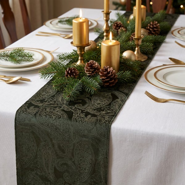 Festlich gedeckter Tisch mit weihnachtlicher Tischdekoration, bestehend aus einem gemusterten Tischläufer, Tannenreisig, Zapfen und Kerzen.