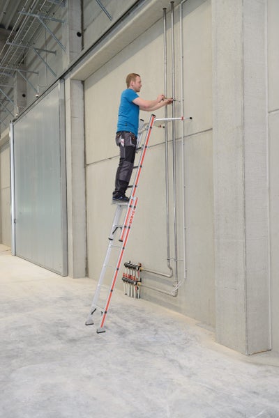 Eine Person arbeitet auf einer Mehrzweckleiter an einer Wand mit Rohren.