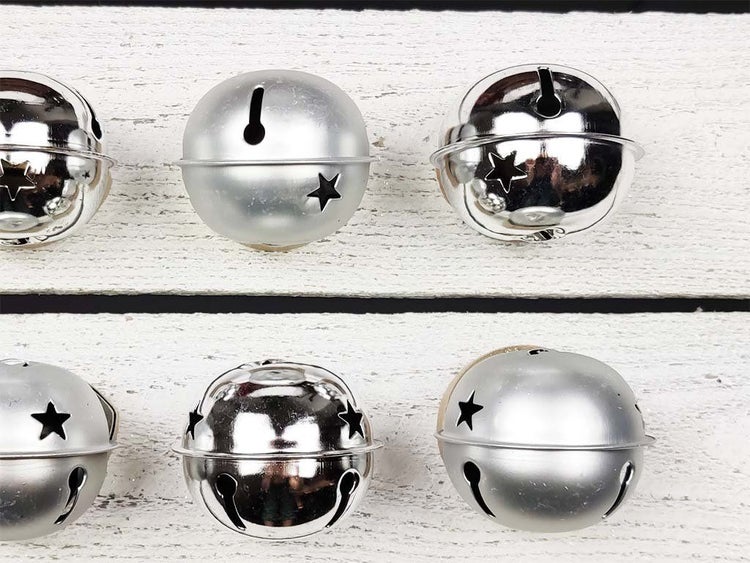 Mehrere metallene Weihnachtsglöckchen mit Sternausschnitten auf weißem Holzuntergrund.