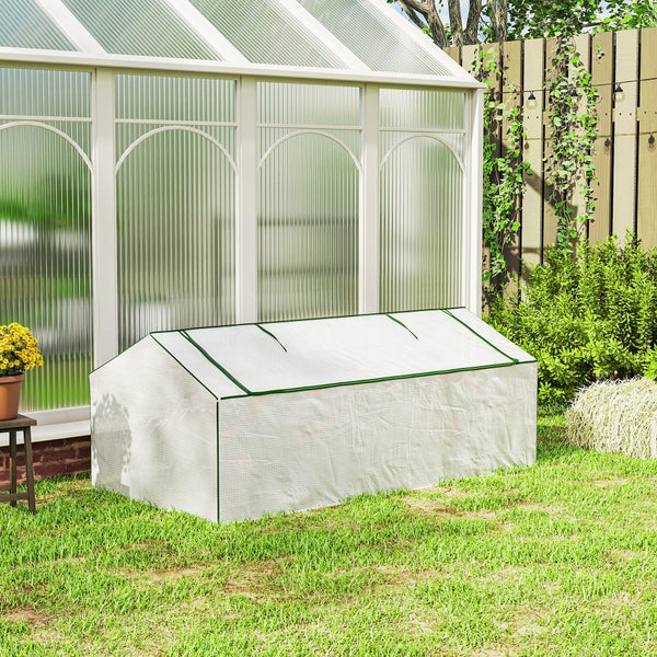 Kleines Foliengewächshaus aus weißem Gittergewebe mit grünem Rand auf einer Rasenfläche im Garten vor einem großen Gewächshaus.