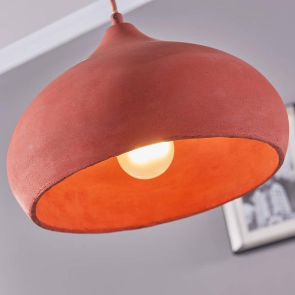 Pendelleuchte aus Beton in Terrakotta mit rundem Schirm und eingeschaltetem Leuchtmittel.