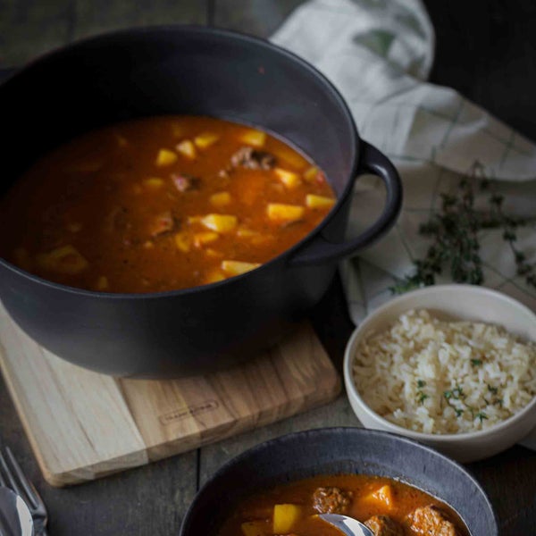 Eintopf mit Fleisch und Kartoffeln in Schüssel und Topf, serviert mit Reis