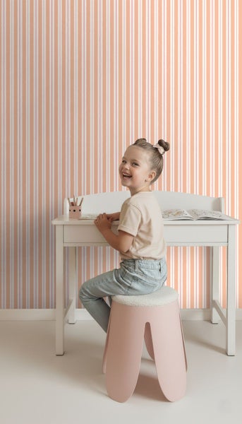 Mädchen sitzt an einem Schreibtisch vor einer Tapete mit Streifenmuster.