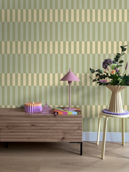 Wohnraumszene mit einer Tapete mit vertikalem Streifenmuster, einem Sideboard aus Holz und einer Blumenvase auf einem Hocker.