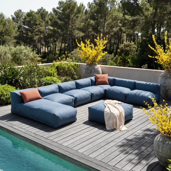 Modulares L-förmiges Outdoor-Lounge-Sofa in Blau auf einer Holzterrasse am Pool mit passendem Hocker und Zierkissen.
