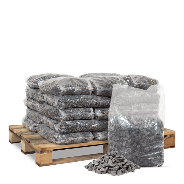 Dunkelgrauer Splitt in transparenten Säcken auf einer Holzpalette gestapelt mit einer kleinen Schüttung im Vordergrund.