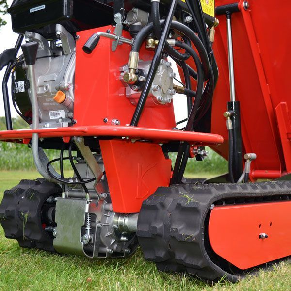 Nahaufnahme eines roten Raupendumpers mit Gummiketten, Motor und Hydrauliksystem auf einer Grasfläche.