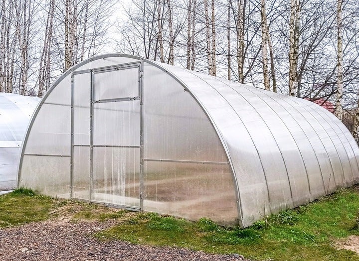 Rundbogengewächshaus aus Polycarbonatplatten mit Metallrahmen und integrierter Tür im Außenbereich.