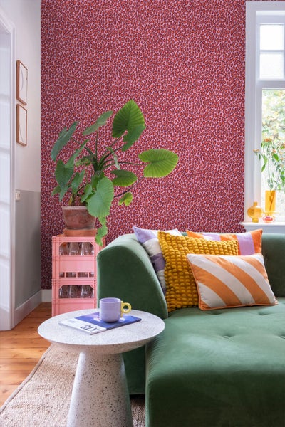 Tapete mit Leopardenmuster in Rosa und Rot in einem farbenfrohen Wohnzimmer mit grüner Couch und Zimmerpflanze.