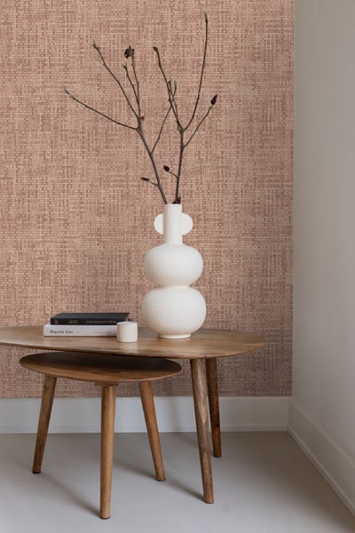 Vliestapete mit Gittermuster in Weboptik an einer Wand hinter einem Holztisch mit weißer Vase und Zweigen.