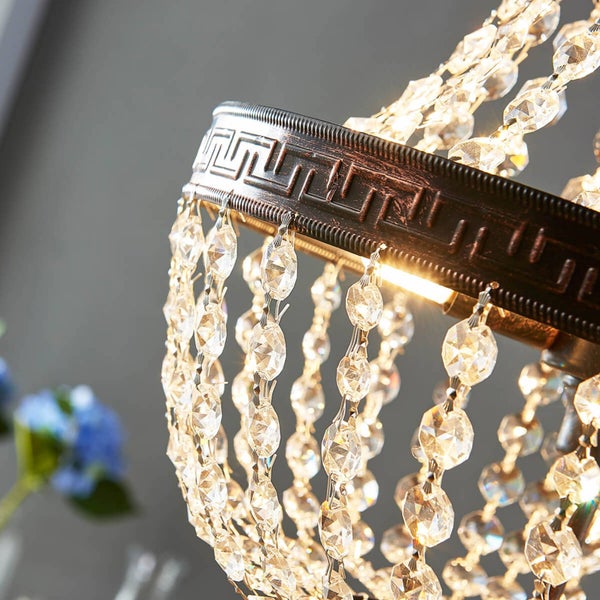 Detailansicht eines Kronleuchters mit metallenem Zierring im Meander-Muster und herabhängenden Ketten aus geschliffenen Kristallen.