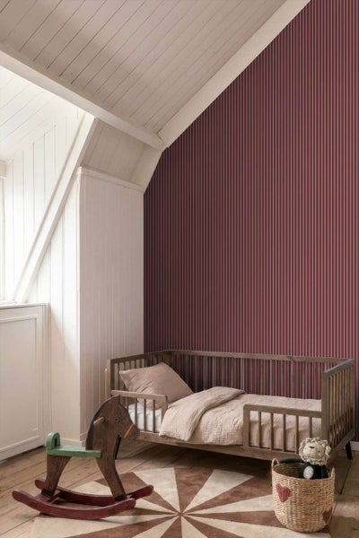 Ein Kinderzimmer mit einer Wand in dunklem Streifenmuster, einem Holzgitterbett, einem Schaukelpferd aus Holz und einem runden Teppich.