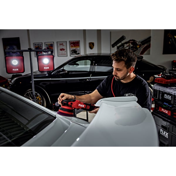 Ein Handwerker nutzt einen Exzenterschleifer der Marke Flex zur professionellen Autopolitur in einer Werkstatt mit mobiler LED Arbeitsleuchte.